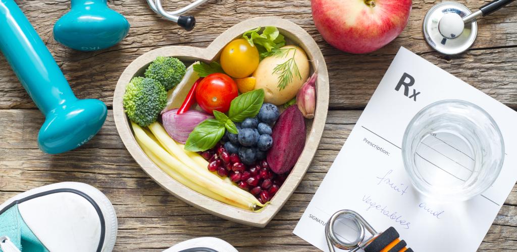 Heart shaped bowl filled with fruits and vegetables along with running shoes and weights