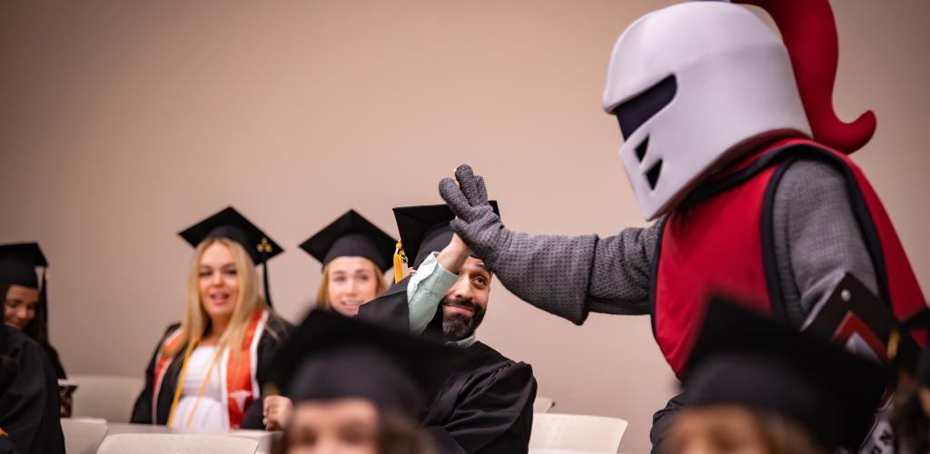 Barry the mascot giving high five to a student wearing cap and gown
