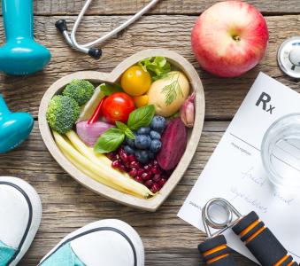 Heart shaped bowl filled with fruits and vegetables along with running shoes and weights