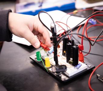 Student's hand plugging a wire into the circuit board 