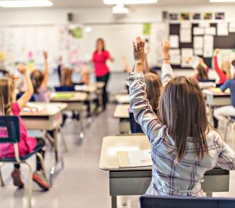 Classroom full of elementary students raising their hands to answer a question