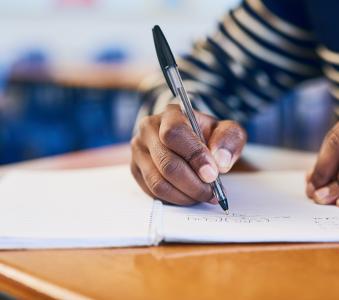 Hands, writing and exam in classroom at university with solution, student and notebook for assessment. Person, test or quiz with question paper, learning and education with scholarship at college