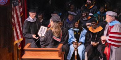 RCBC student being handed an award on stage at commencement (photo has crayon filter applied)