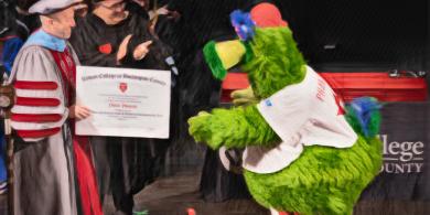 President Cioce handing Philly Phanatic his diploma on stage (photo has crayon filter applied)