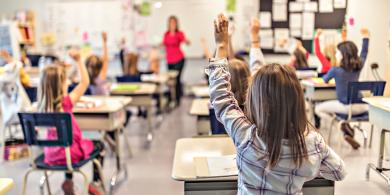 Classroom full of elementary students raising their hands to answer a question