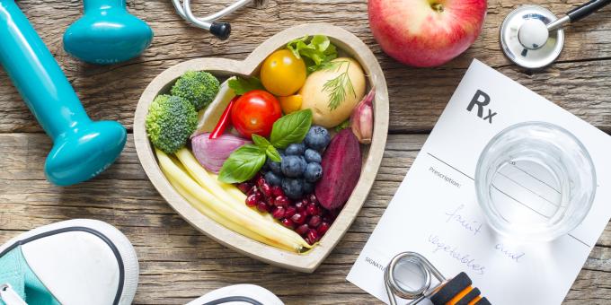 Heart shaped bowl filled with fruits and vegetables along with running shoes and weights