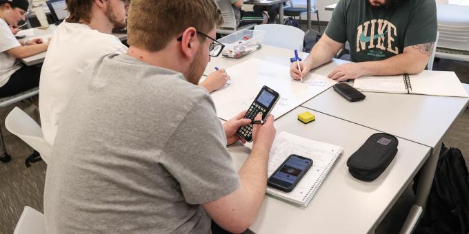 RCBC students work together on a problem in class with calculators and white boards.