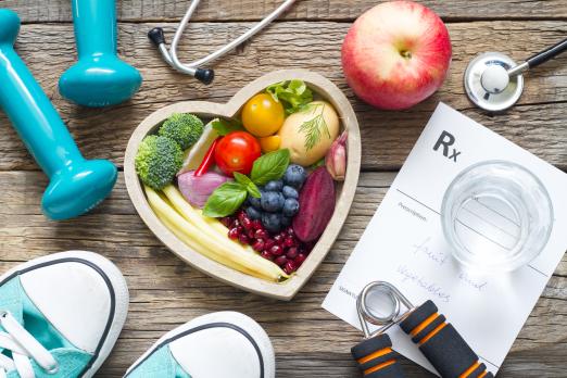 Heart shaped bowl filled with fruits and vegetables along with running shoes and weights