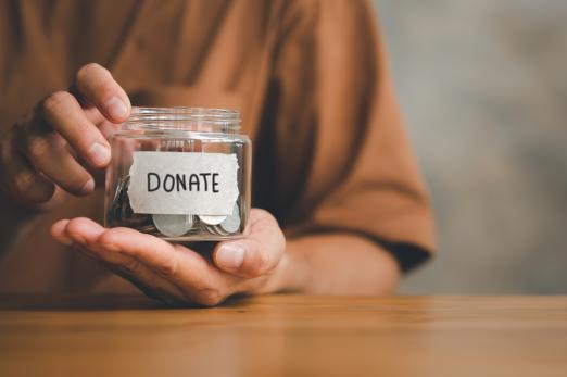 A pair of hands holding a coin jar with labeled donate
