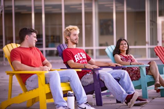 Three RCBC students sitting in bold colored Adirondack chairs