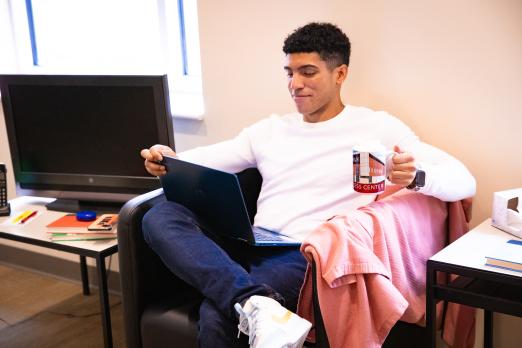 RCBC student holding hot chocolate while working on a lap top