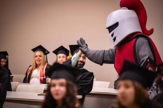 Barry the mascot giving high five to a student wearing cap and gown