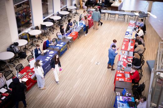 Various college university tables lined up the SSC lobby for Transfer Fair. 