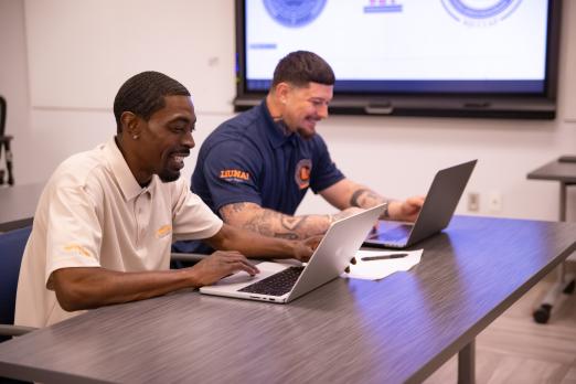 Two LIUNA members sit at laptops side-by-side.