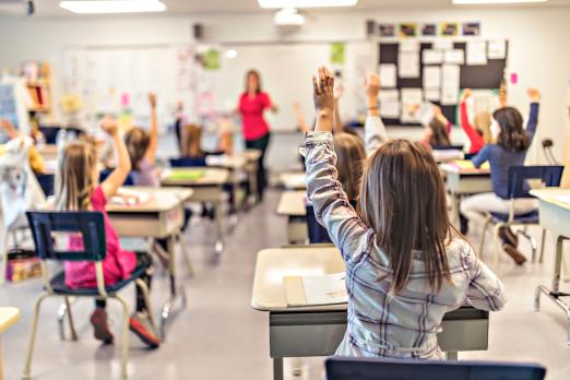 Classroom full of elementary students raising their hands to answer a question