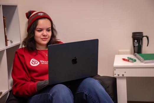 Female RCBC student dressed in winter gear in the corner using a laptop 