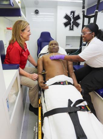 An instructor guides a student in an ambulance simulation