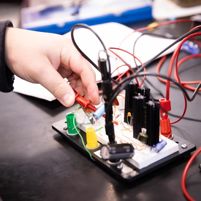 Student's hand plugging a wire into the circuit board 