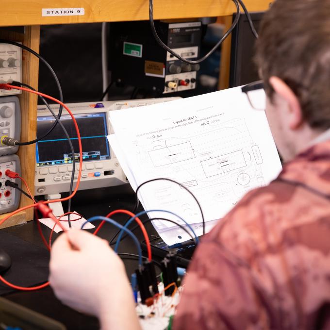 Student holding wires and reading electrical engineering diagram 