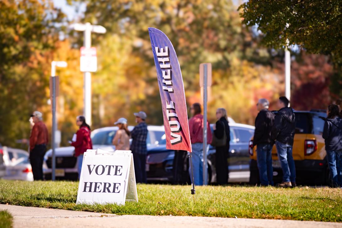 Prospective voters stand in a line behind two signs that read "Vote Here".